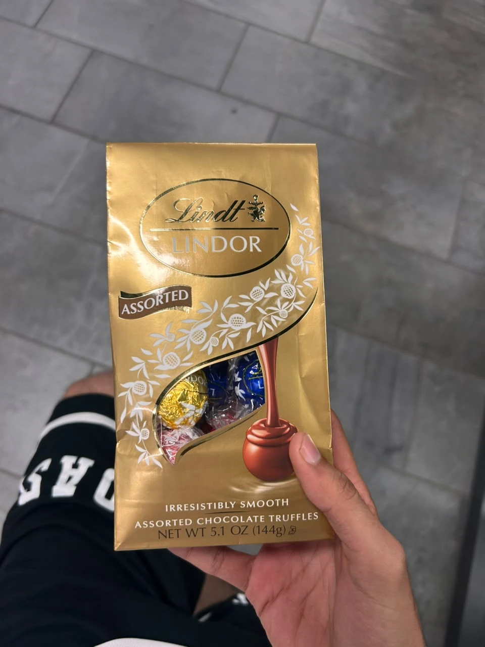 A gold bag of Lindt Lindor assorted chocolate truffles held in one hand